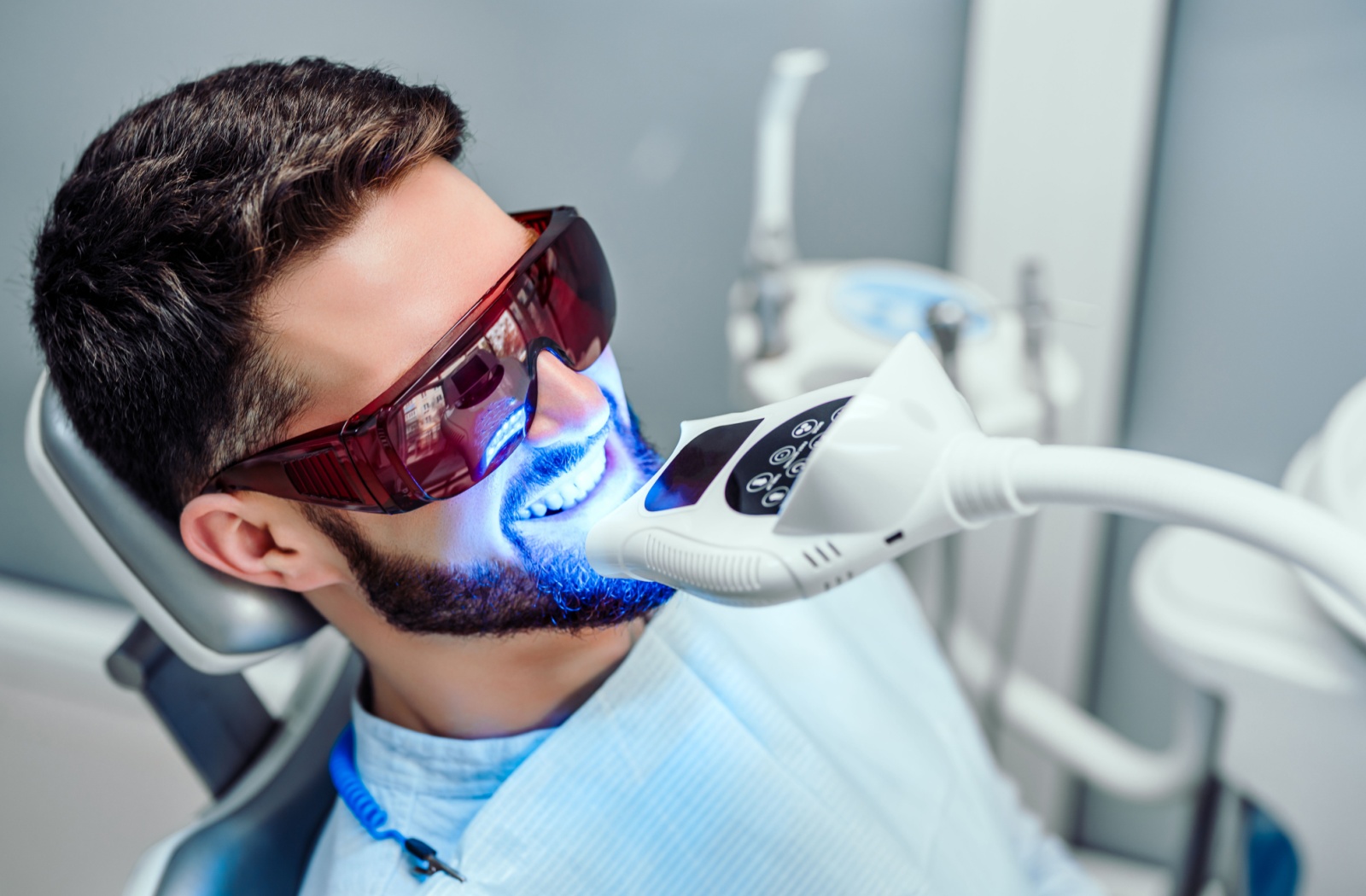 An adult wearing shaded glasses undergoes an in-office teeth whitening treatment.