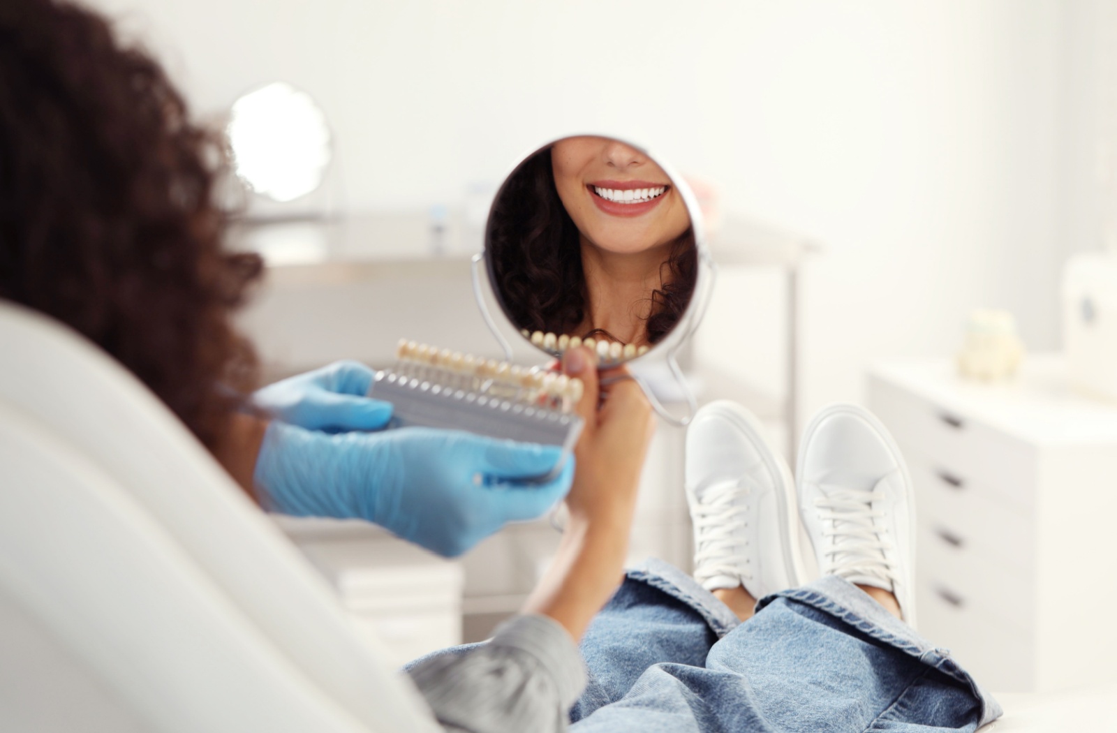 Patient sitting in a dental office smiling into a mirror while comparing tooth colours for veneers.