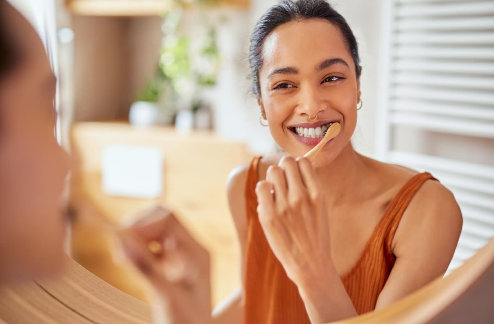 Person brushing their teeth with a bamboo toothbrush while looking into a mirror in a bright, modern bathroom. 
