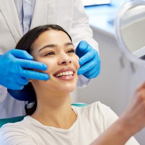 A woman smiles into a hand mirror after her teeth whitening appointment.