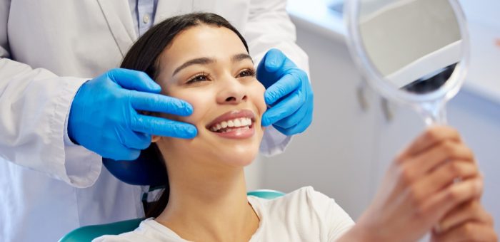 A woman smiles into a hand mirror after her teeth whitening appointment.