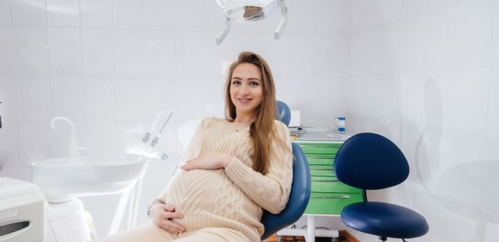 A pregnant woman sitting comfortably in a dental chair, smiling during her dental checkup.