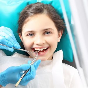 A child sits in a dental chair while their dentist cleans their teeth.