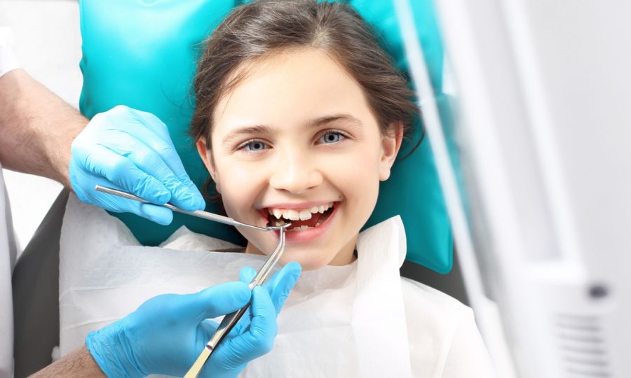 A child sits in a dental chair while their dentist cleans their teeth.