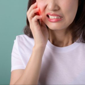 A woman holding her jaw due to tooth pain from a cavity.