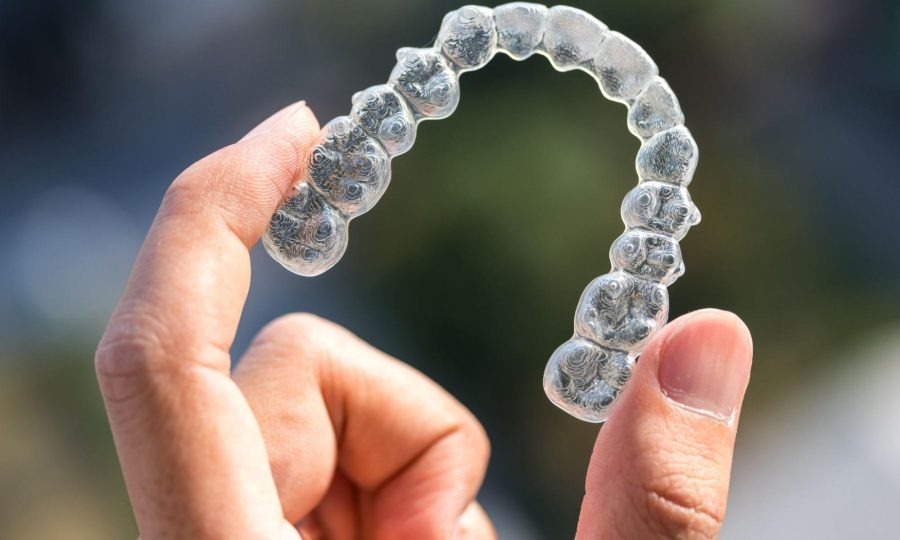 A person holding an Invisalign aligner between their left thumb and index fingers.