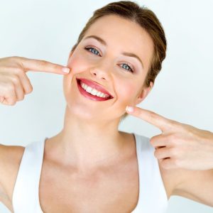 A woman smiling and pointing at her shiny white teeth